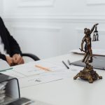 Estátua da Justiça ao lado de documentos e um computador em uma mesa de trabalho jurídico