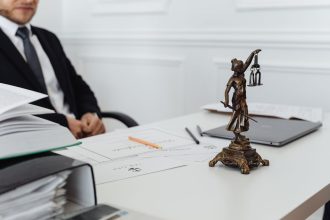 Estátua da Justiça ao lado de documentos e um computador em uma mesa de trabalho jurídico