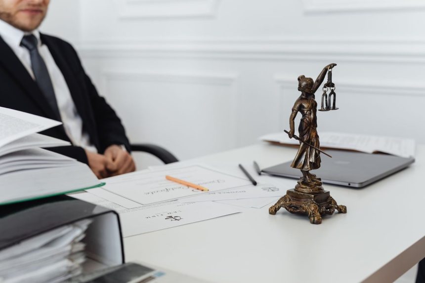 Estátua da Justiça ao lado de documentos e um computador em uma mesa de trabalho jurídico