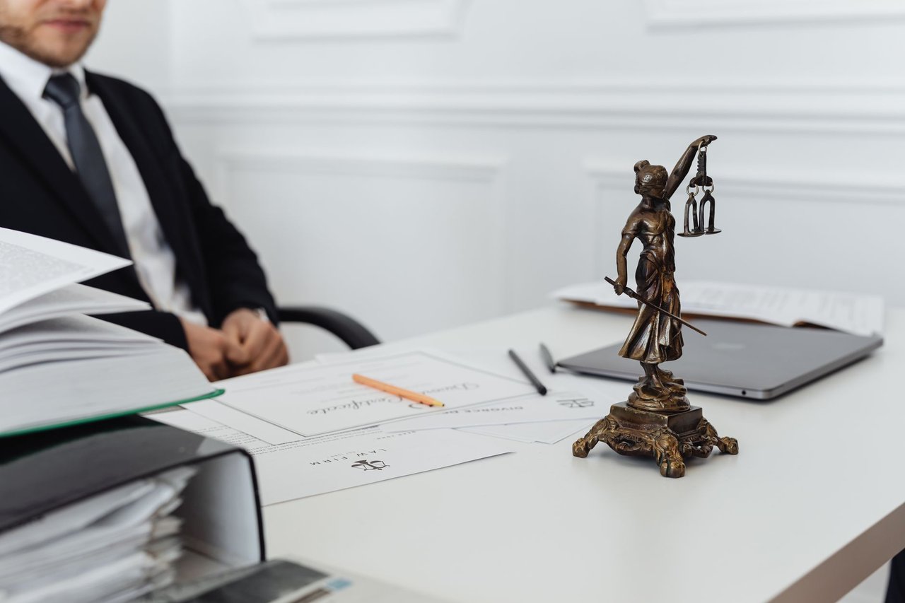 Estátua da Justiça ao lado de documentos e um computador em uma mesa de trabalho jurídico