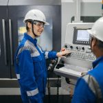 Dois trabalhadores usando equipamentos de proteção operam uma máquina em uma fábrica.