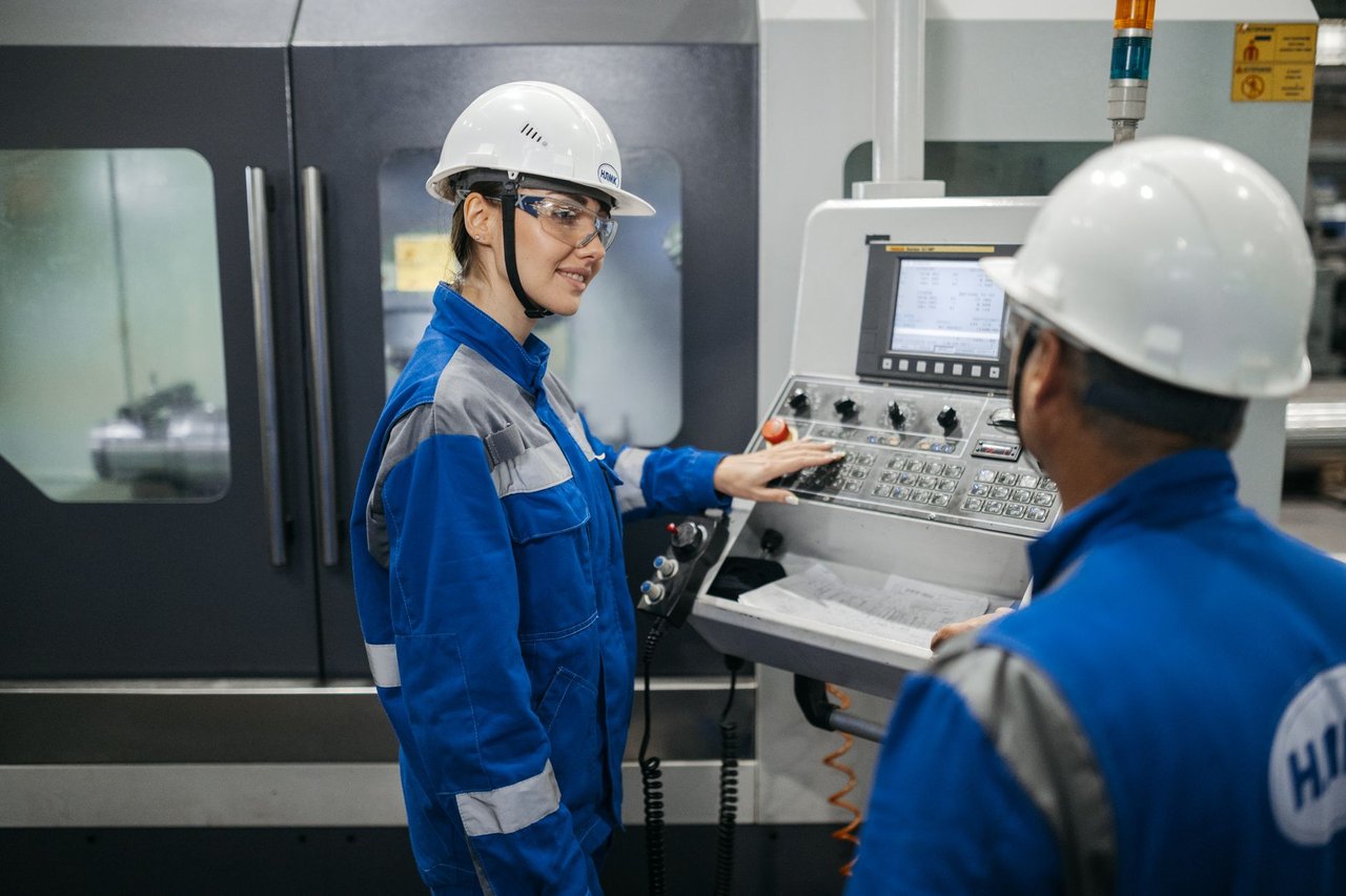 Dois trabalhadores usando equipamentos de proteção operam uma máquina em uma fábrica.